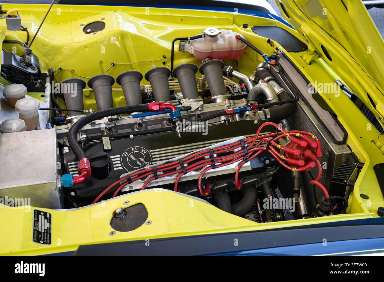 Detail eines klassischen BMW 3,0 CSL-Rennmotors mit zwei Geschwindigkeitsstufen und einem roten Zündverteiler in einem leuchtend gelben Gehäuse Stockfoto