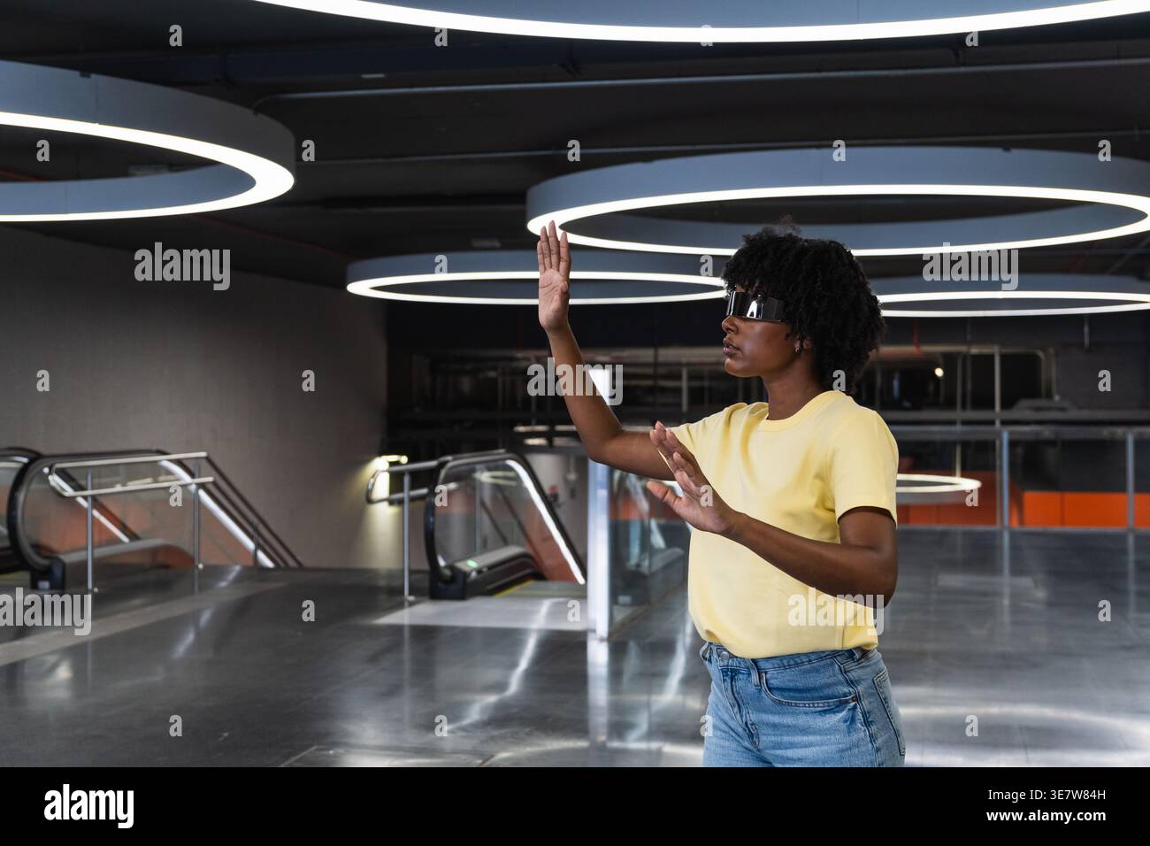 Schwarze Frau mit Afro, die eine futuristische, intelligente Brille trägt, während sie in einem Gebäude steht Stockfoto
