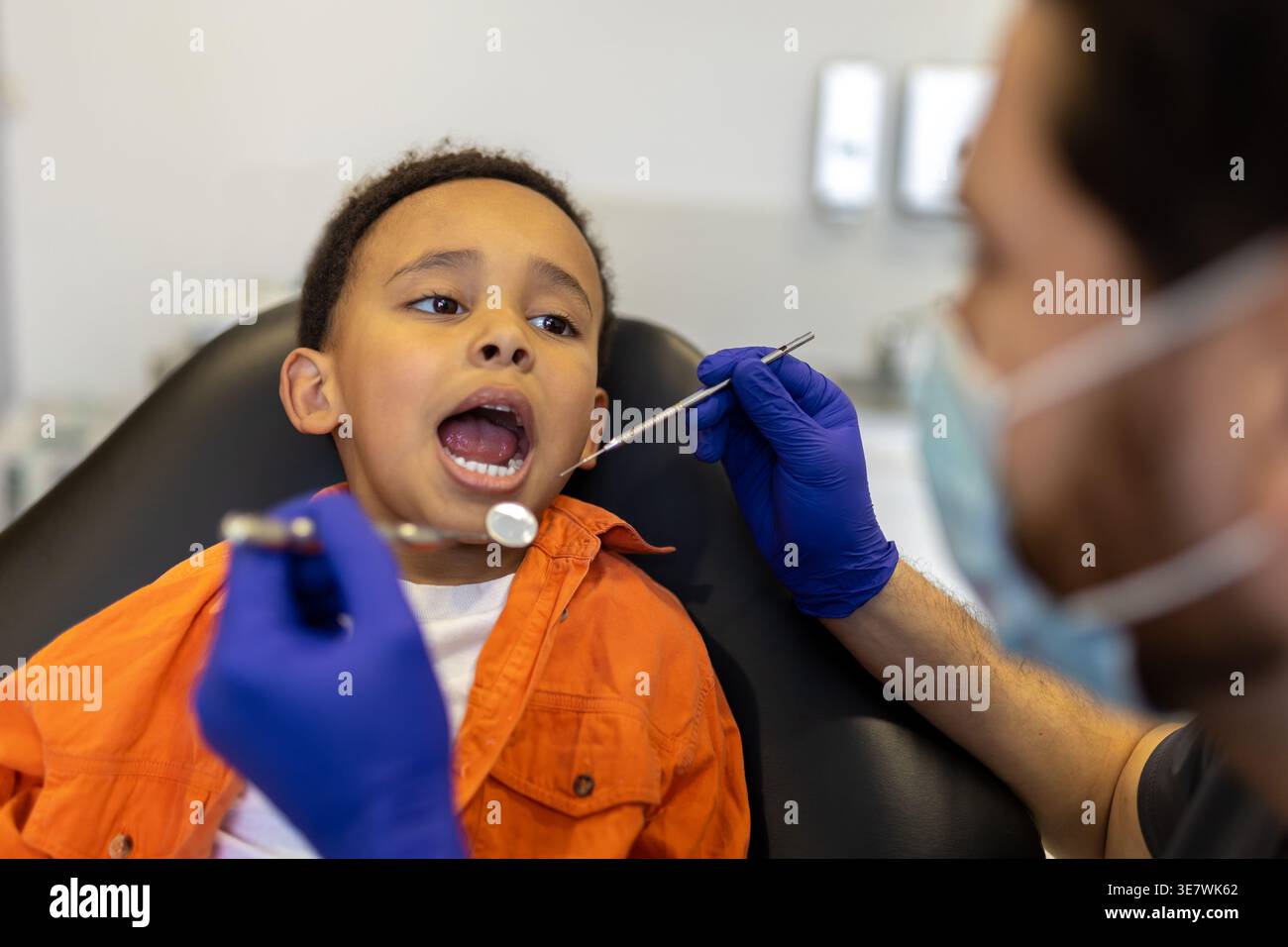 Schwarzer Junge bei zahnärztlicher Behandlung mit kaukasischem Zahnarzt in der Klinik Stockfoto