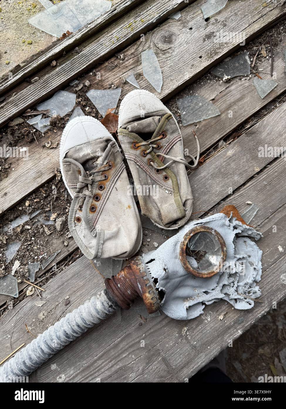 Verlassene Turnschuhe und Gasmaske auf kaputtem Holzboden Stockfoto