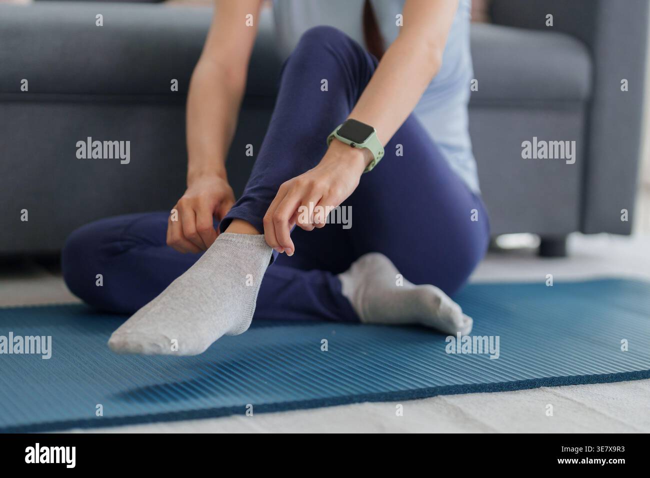 Asiatische Erwachsene Frau sitzt auf einer Yogamatte und bereitet sich auf das Training vor. Sie passt ihre sportliche Socke an, um die Bereitschaft zum Training zu demonstrieren Stockfoto