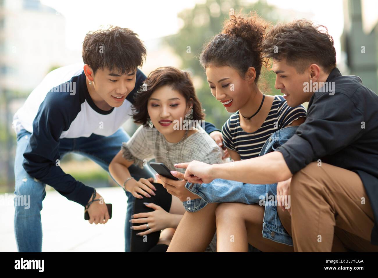 Lächelnde Gruppe chinesischer Freunde, die tagsüber auf der Straße sitzen Stockfoto