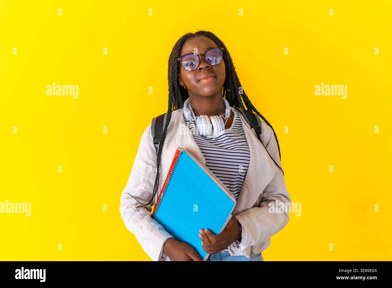 Schwarze Teenagerin mit Brille, die Bücher vor gelbem Hintergrund im Studio hält Stockfoto
