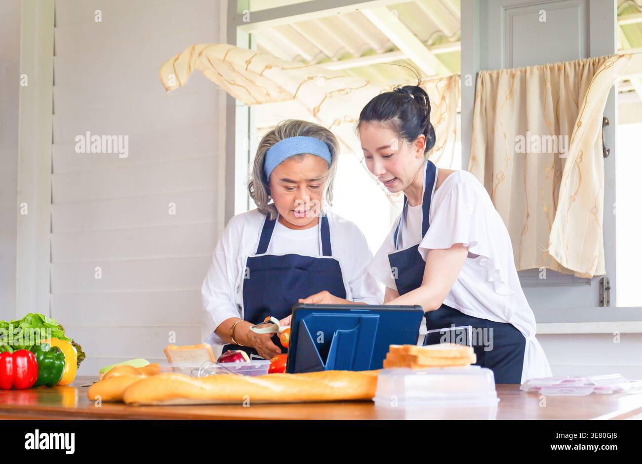 Asiatische Frau mittleren Alters, die Essen zubereitete, mit einer älteren Mutter, die in der Küche am Tisch stand Stockfoto