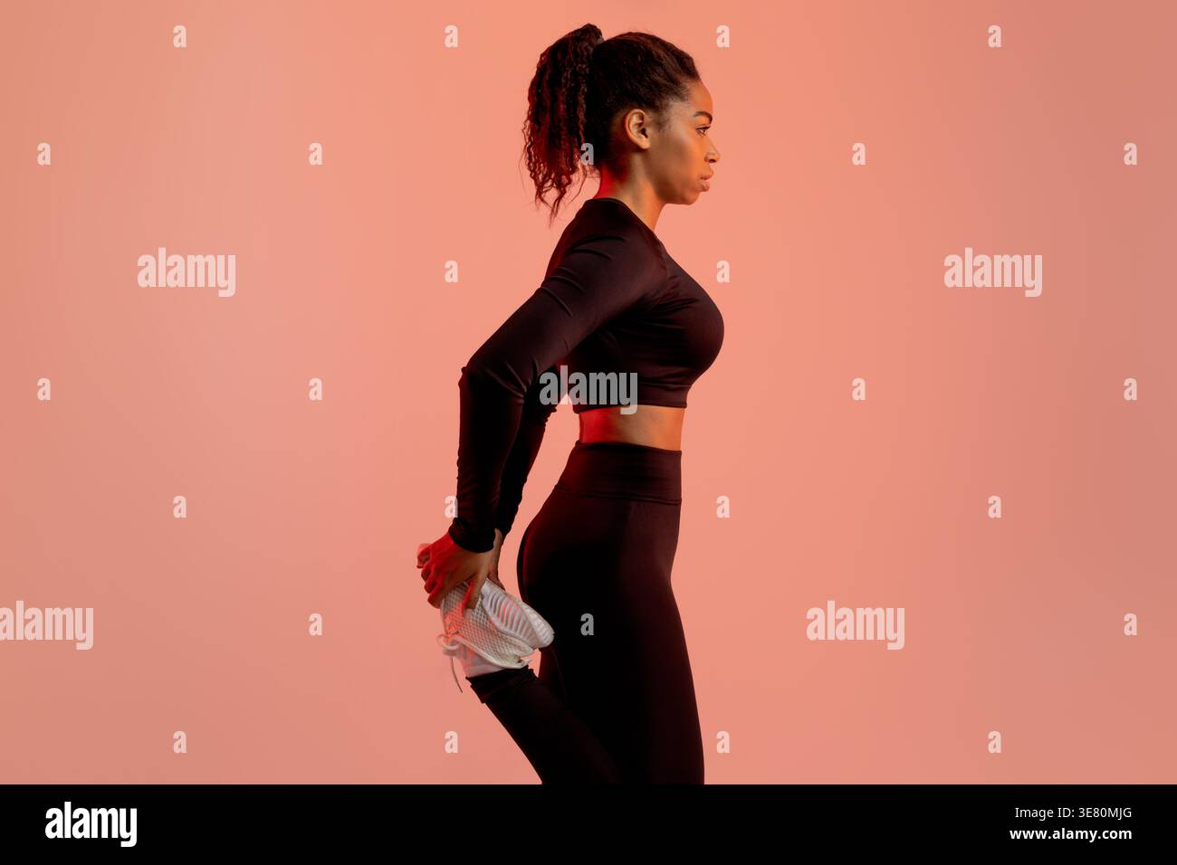 Schwarze Frau mit Sportbekleidung, das Bein vor rosa Hintergrund im Studio dehnt Stockfoto