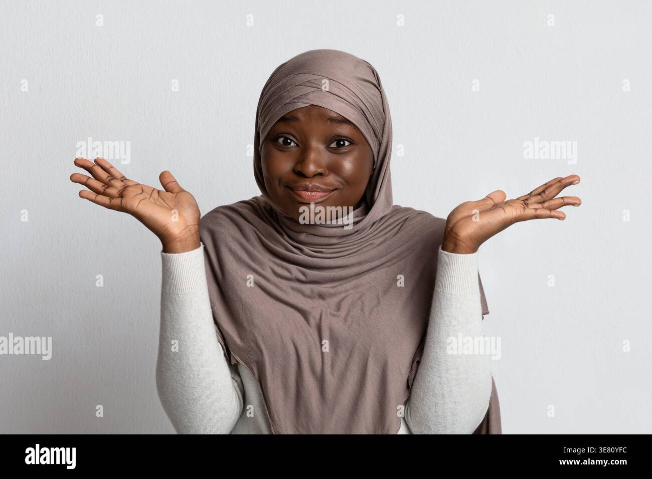 Enttäuschte schwarze muslimische Frau im Hijab, die Hände vor grauem Hintergrund im Atelier spreizt Stockfoto