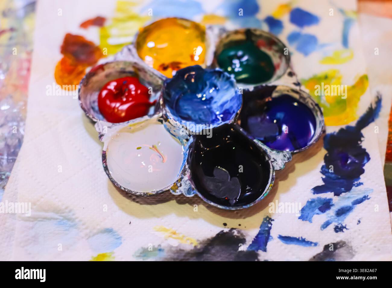 Nahaufnahme einer unordentlichen Künstlerpalette mit leuchtenden Ölfarben auf Papier. Authentischer Arbeitsbereich für Kunstunterricht und kreativen Hobbyhintergrund. Stockfoto