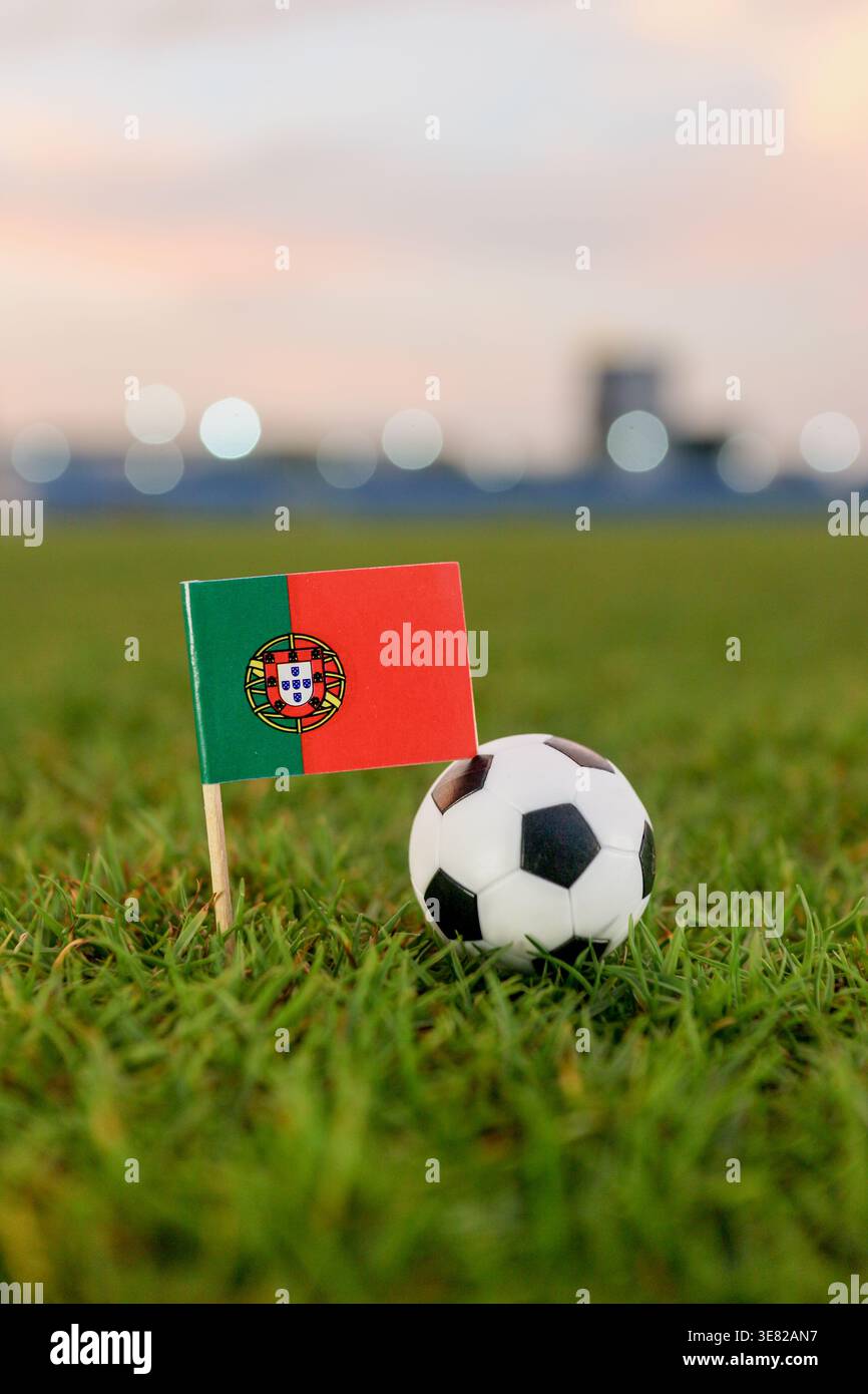 Portugal Flaggenaufnäher und Fußball auf Stadionrasen bei Sonnenuntergang. Symbolische Bilder des Weltturniers mit orangefarbenem Himmel und unscharfen Bokeh-Lichtern. Stockfoto