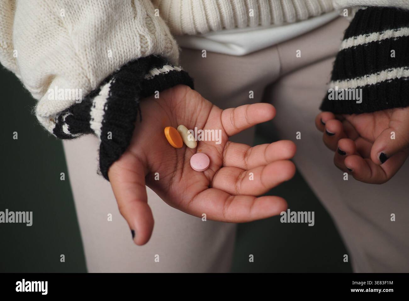 Ein Kind zeigt drei unterschiedlich farbige Pillen in der Hand in einem Raum Stockfoto