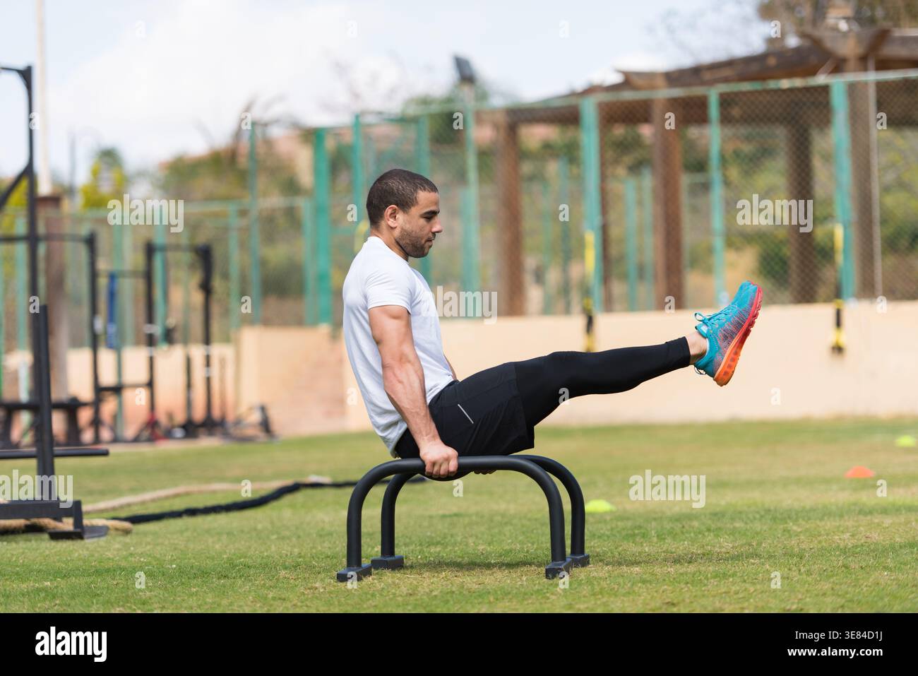 Sportlicher Mann, der beim CrossFit Workout im Freien L-Sit auf parallelen Bars durchführt Stockfoto