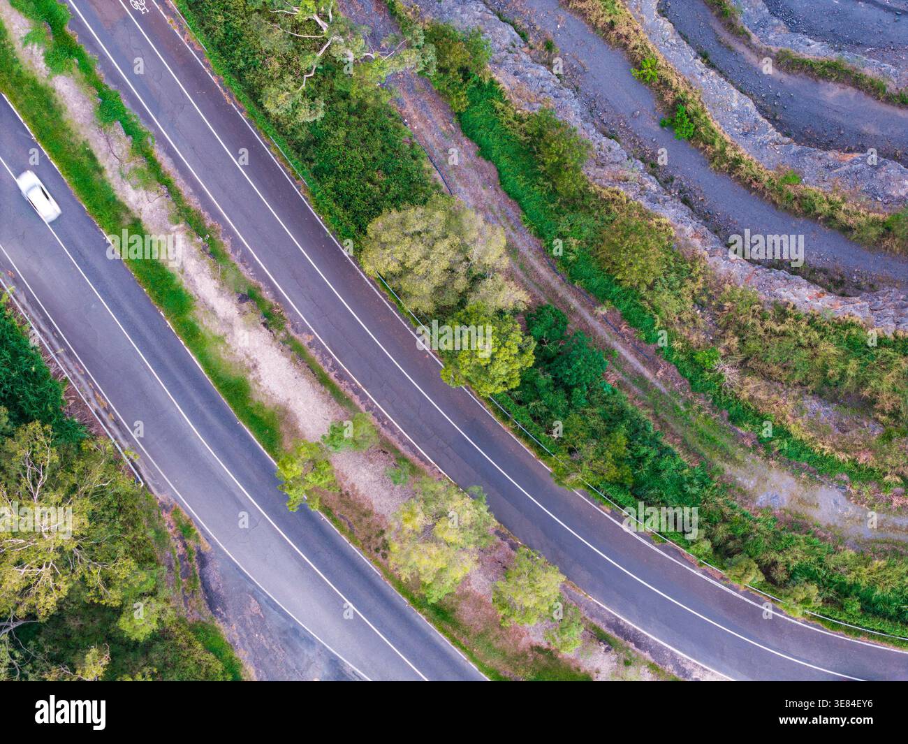 Ein Blick von oben zeigt eine mehrspurige Straße, die sich durch üppige Vegetation und entlang eines gemeißelten Felsendamms in Brisbane schlängelt. Stockfoto