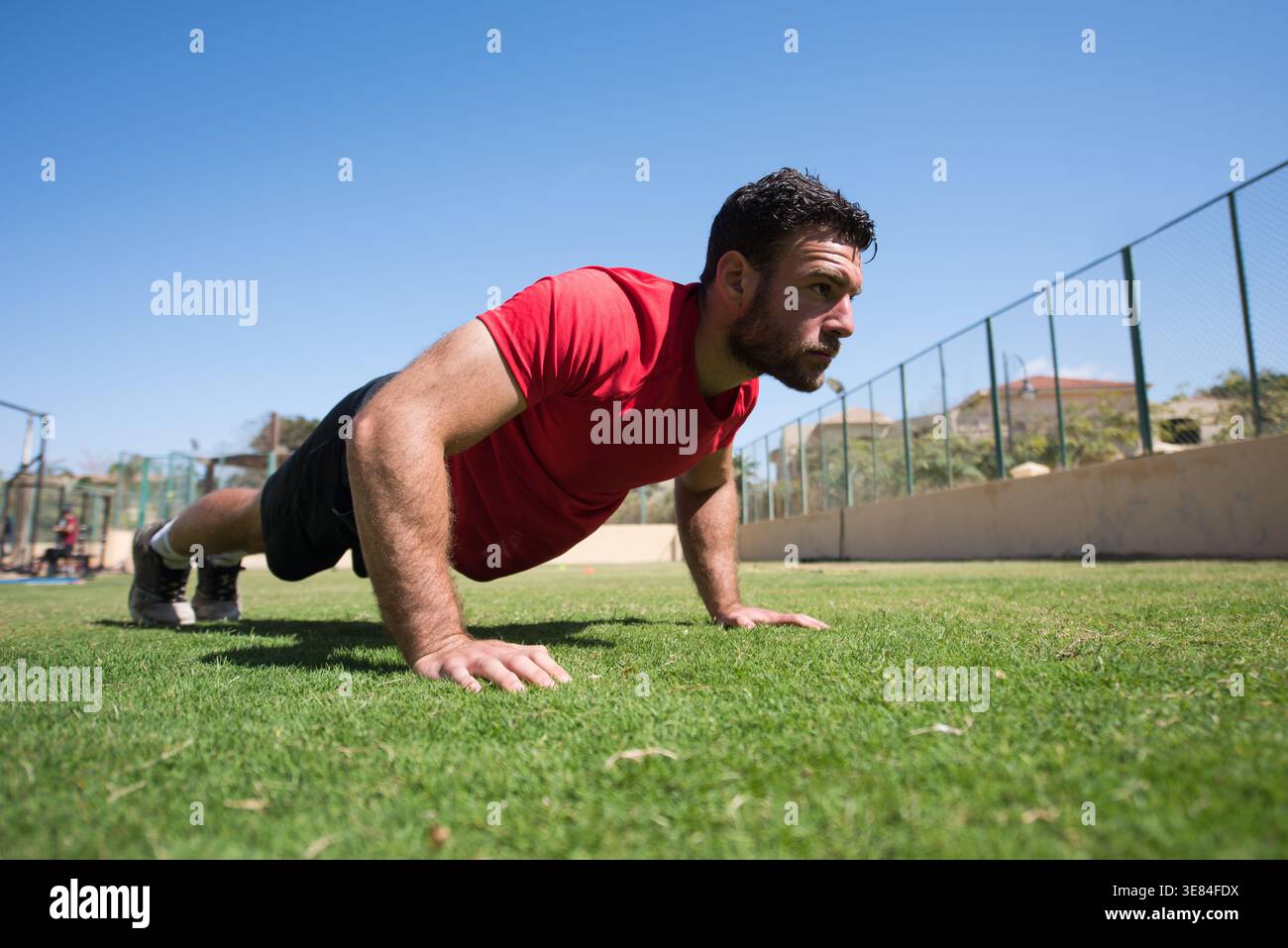 Mann, der Liegestütze im Freien in einem CrossFit-Fitness-Studio mit fokussiertem Ausdruck macht Stockfoto