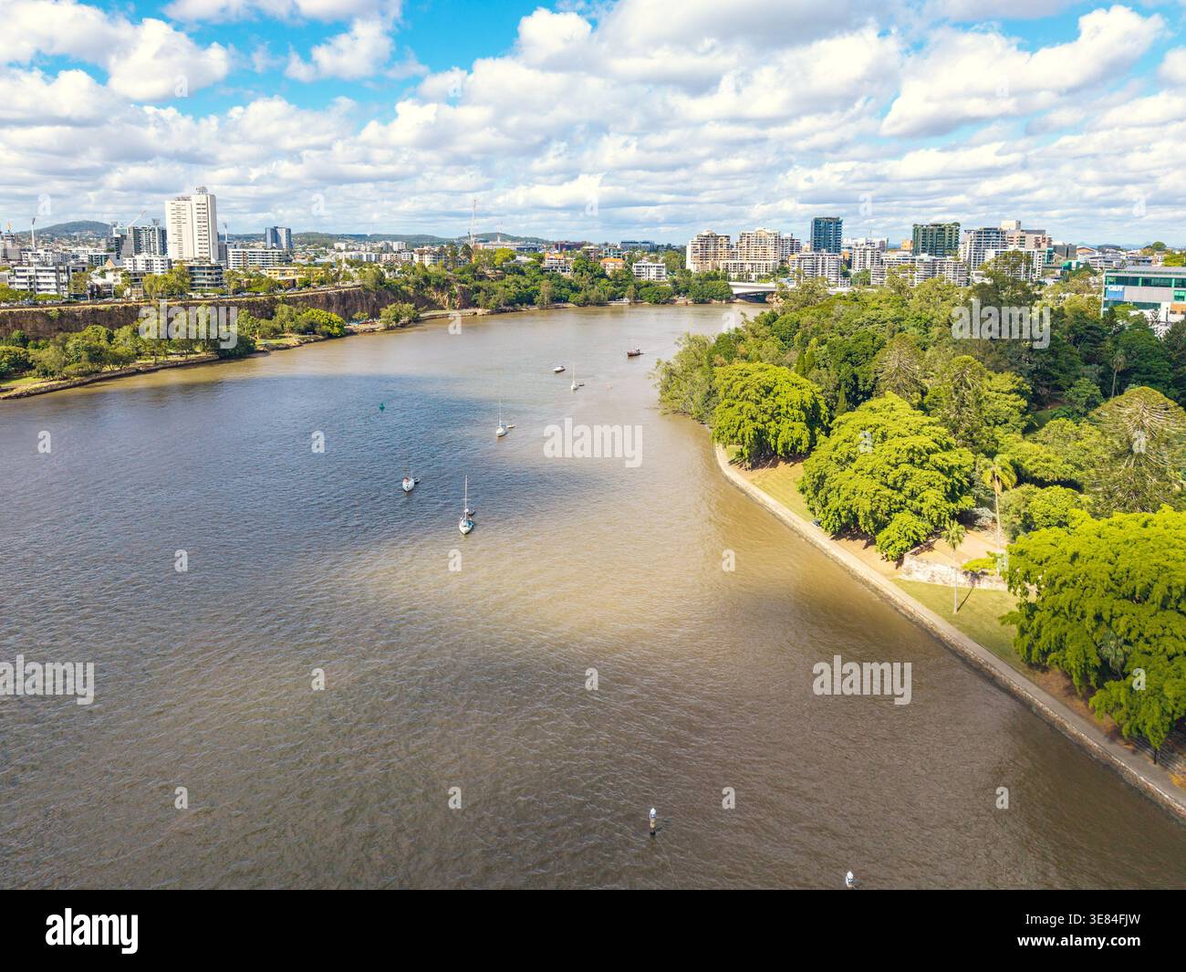 Der Brisbane River fließt vorbei an urbanen Hochhäusern und grünen Parklandschaften, die ein auffälliges zweifarbiges Wasserphänomen mit mehreren Segelbooten bieten. Stockfoto