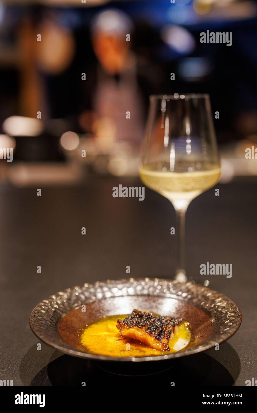 Feine Speiseszene mit Gourmet-Fisch und einem Glas Weißwein auf einem dunklen Tisch, geringer Tiefe des Feldes und warmer Bokeh-Beleuchtung im Restaurant Stockfoto