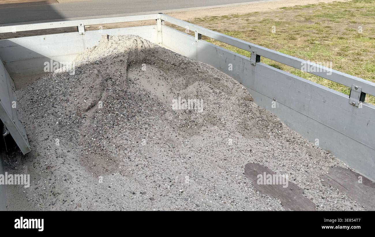Kies- und Sandhaufen auf der Rückseite eines Lkw-Bettes auf einer Baustelle mit einer grasbewachsenen Fläche und einer im Hintergrund sichtbaren Straße Stockfoto