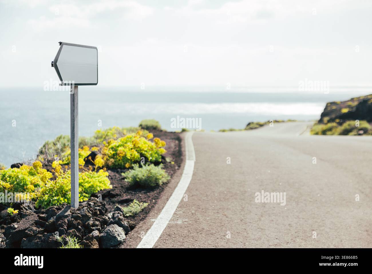 Leeres Straßenschild neben einer ruhigen Küstenstraße, gesäumt von vulkanischen Felsen und gelben Blumen, mit Blick auf den Atlantischen Ozean auf La Palma, Kanarische Insel Stockfoto
