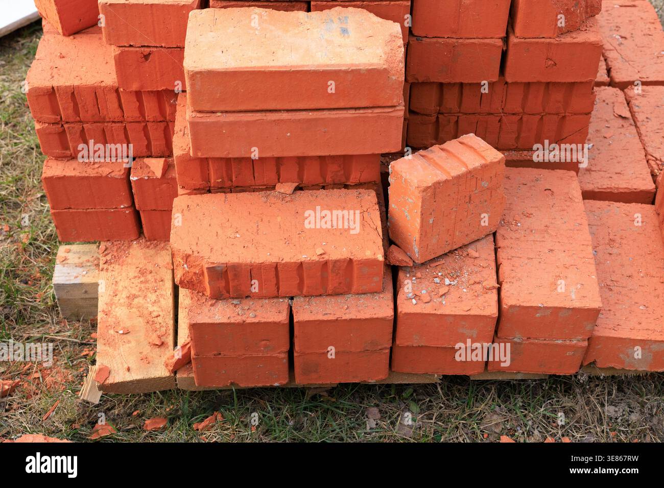 Ordentlicher Stapel roter Tonziegel auf einer Holzpalette auf einer Außenbaustelle. Langlebige Keramikmauerblöcke, die für den Wandbau und die Renovierung von Häusern geeignet sind Stockfoto