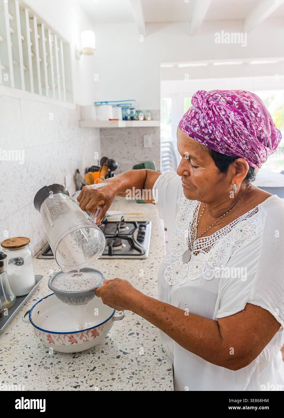 Eine Frau in einem lebendigen Kopftuch bereitet frische Kokosmilch in einer tropischen karibischen Küche zu. Bei diesem Prozess wird eine Mischung aus Kokosnussmischungen für Autom gesaugt Stockfoto