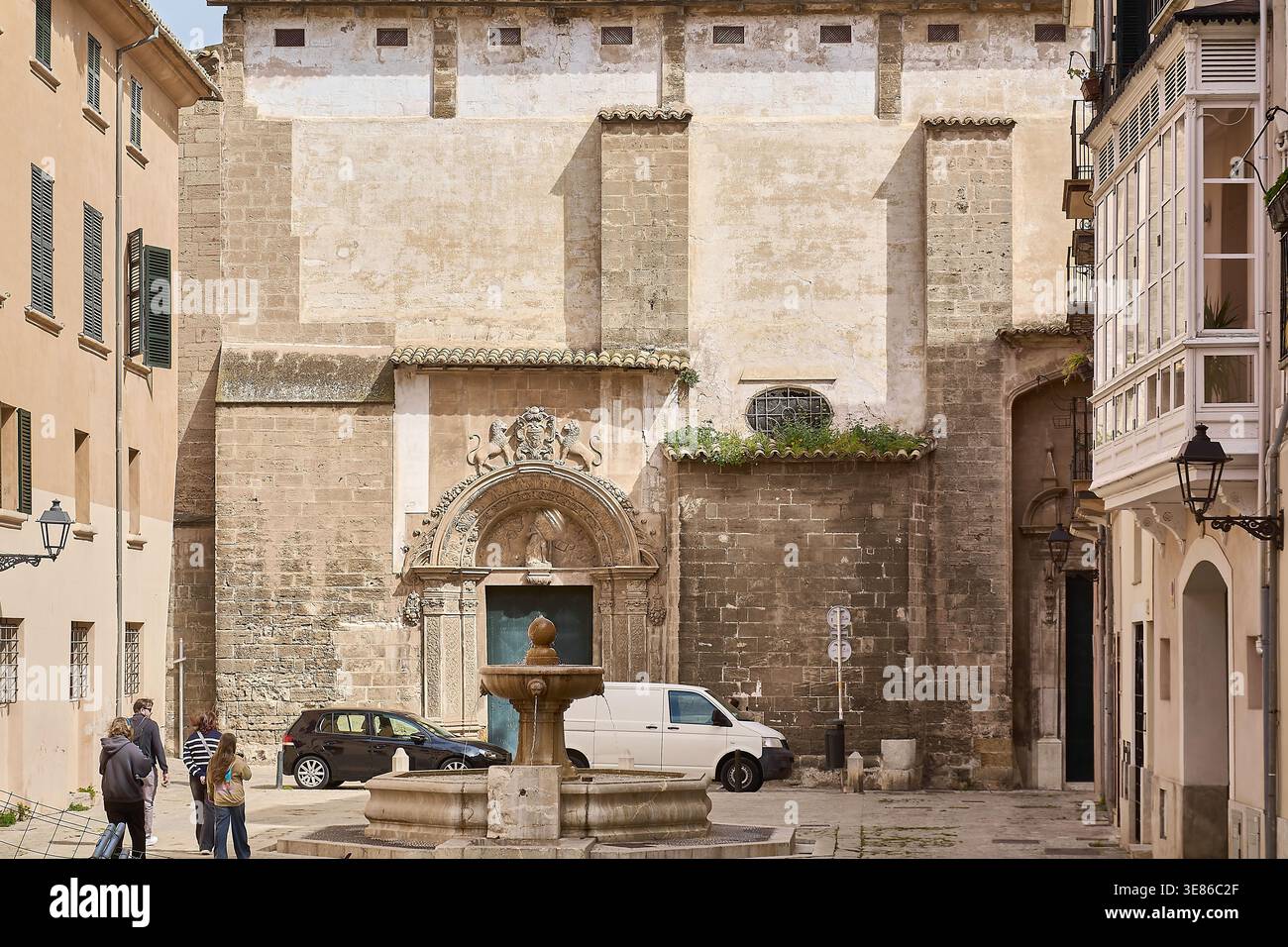 Mallorca. Spanien - 12. April 2026: Touristen gehen an der historischen Esglesia de Sant Jaume und einem Steinbrunnen auf einem sonnigen mediterranen plaza mit tra vorbei Stockfoto