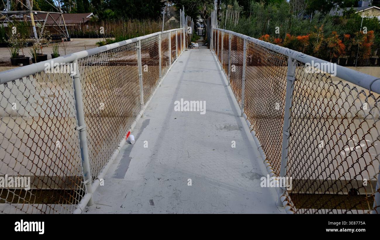 Verwitterte Fußgängerbrücke mit verrostetem Maschendrahtzaun über einem Hochwasserschutzkanal in Reseda, San Fernando Valley, Los Angeles, Kalifornien. Stockfoto