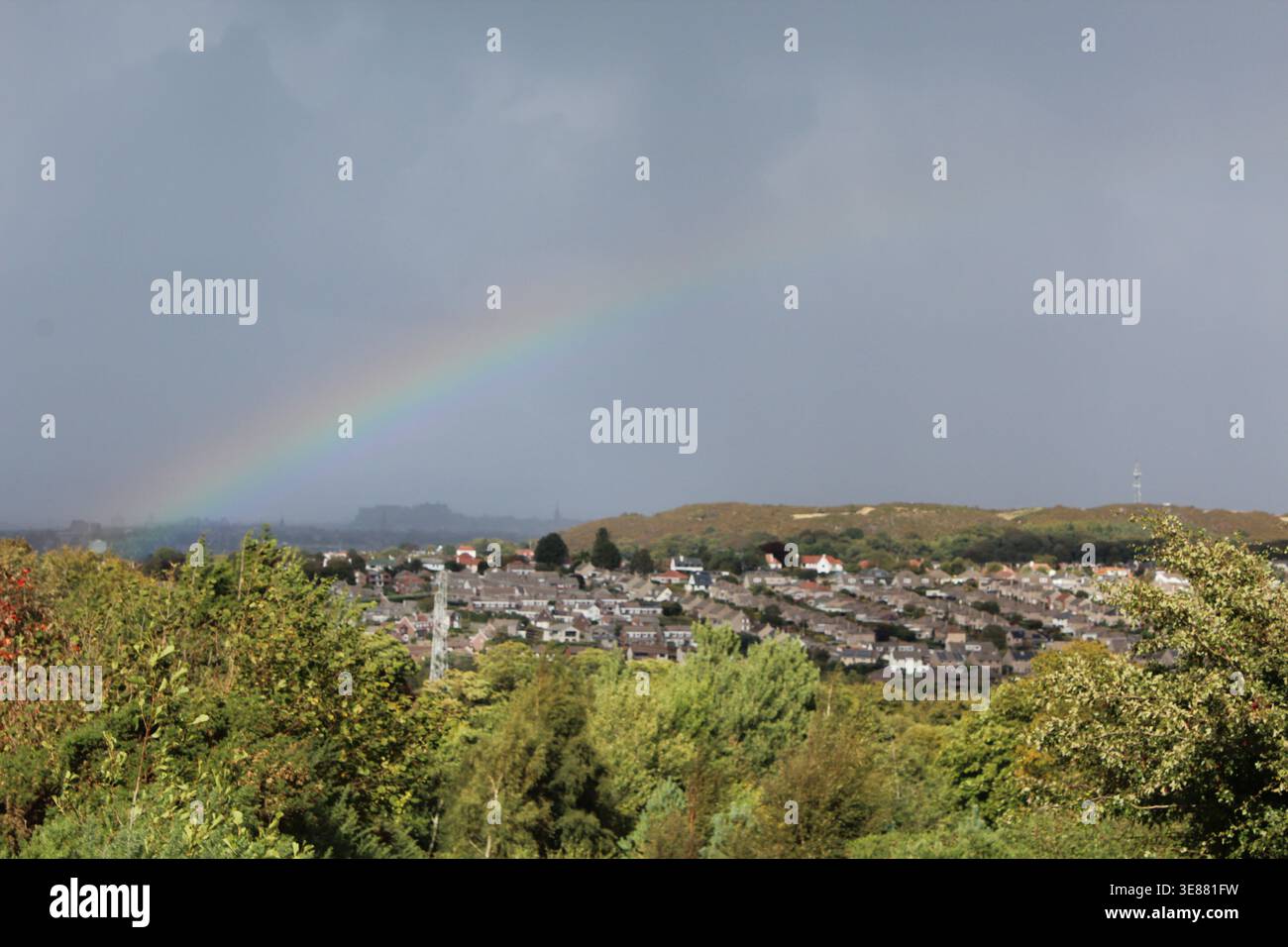 Ein heller Regenbogen, der sich über einen Wohnvorort in Edinburgh, Schottland, erstreckt, vor einem dramatischen, stürmischen, grauen Himmel. Stockfoto