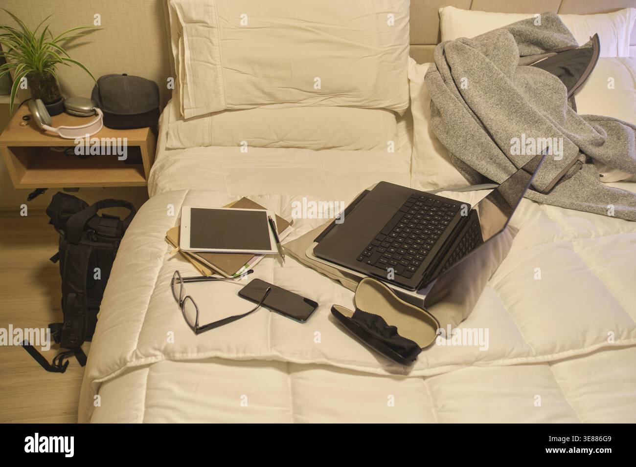 Das Bett dient als unordentliches Heimbüro mit Geräten und Notizen für die Fernarbeit Stockfoto