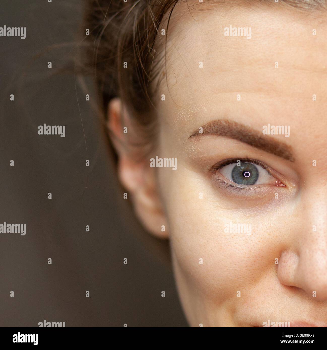 Nahaufnahme eines Porträts einer jungen Frau mit hellbraunem Haar und blauen Augen, das natürliche Schönheit und minimales Make-up vor einem verschwommenen Hintergrund zeigt Stockfoto