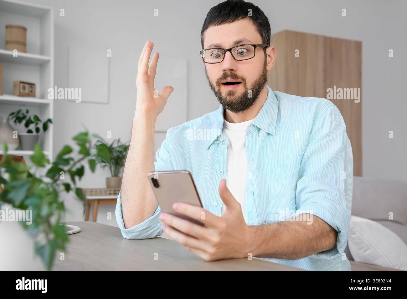 Überraschter junger Mann, der zu Hause ein Handy benutzt Stockfoto