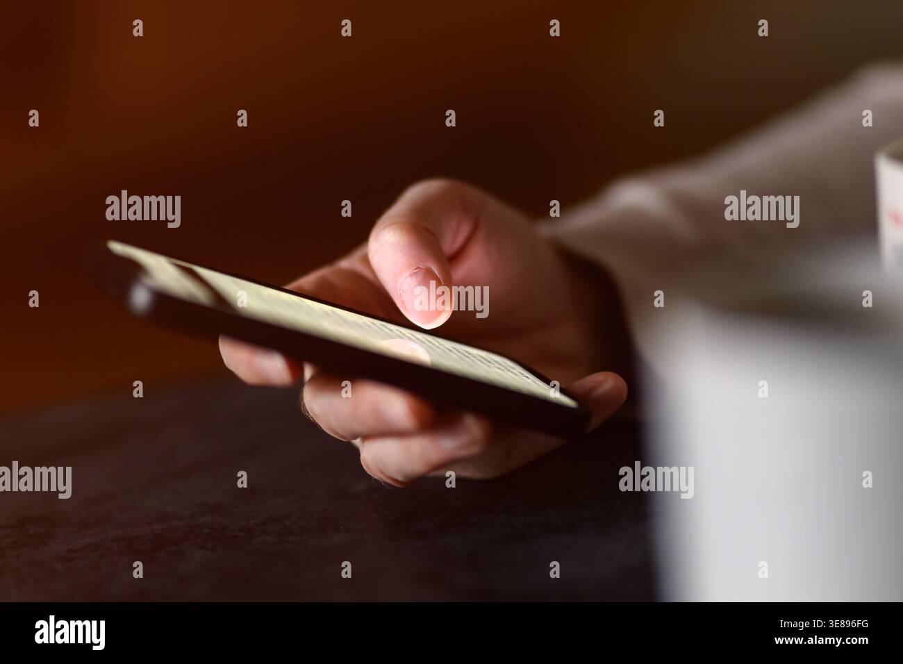 Nahaufnahme der Hand mit Smartphone für SMS und Browsing mit Kaffee bei warmem Licht, selektiver Fokus Stockfoto