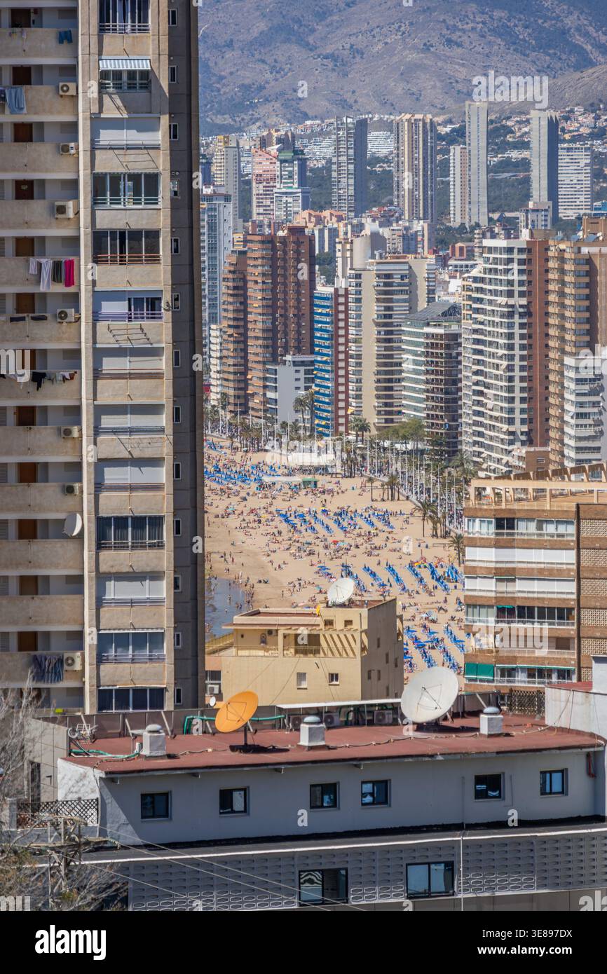 Überfüllter mediterraner Strand in Benidorm, Spanien, durch dichte städtische Wolkenkratzer gesehen Stockfoto