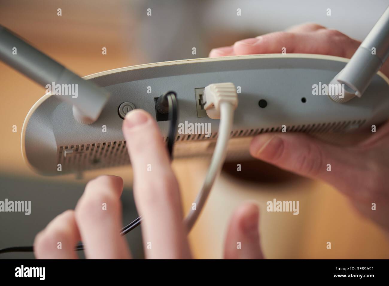 Nahaufnahme der Hände von Erwachsenen, die Kabel mit dem Wireless-Router verbinden, durch Drücken der ein-/Ausschalttaste für die Interneteinrichtung und die Installation des Heimnetzwerks. Nützlich für Breitband, technischen Support und Konnektivitätsanzeigen Stockfoto
