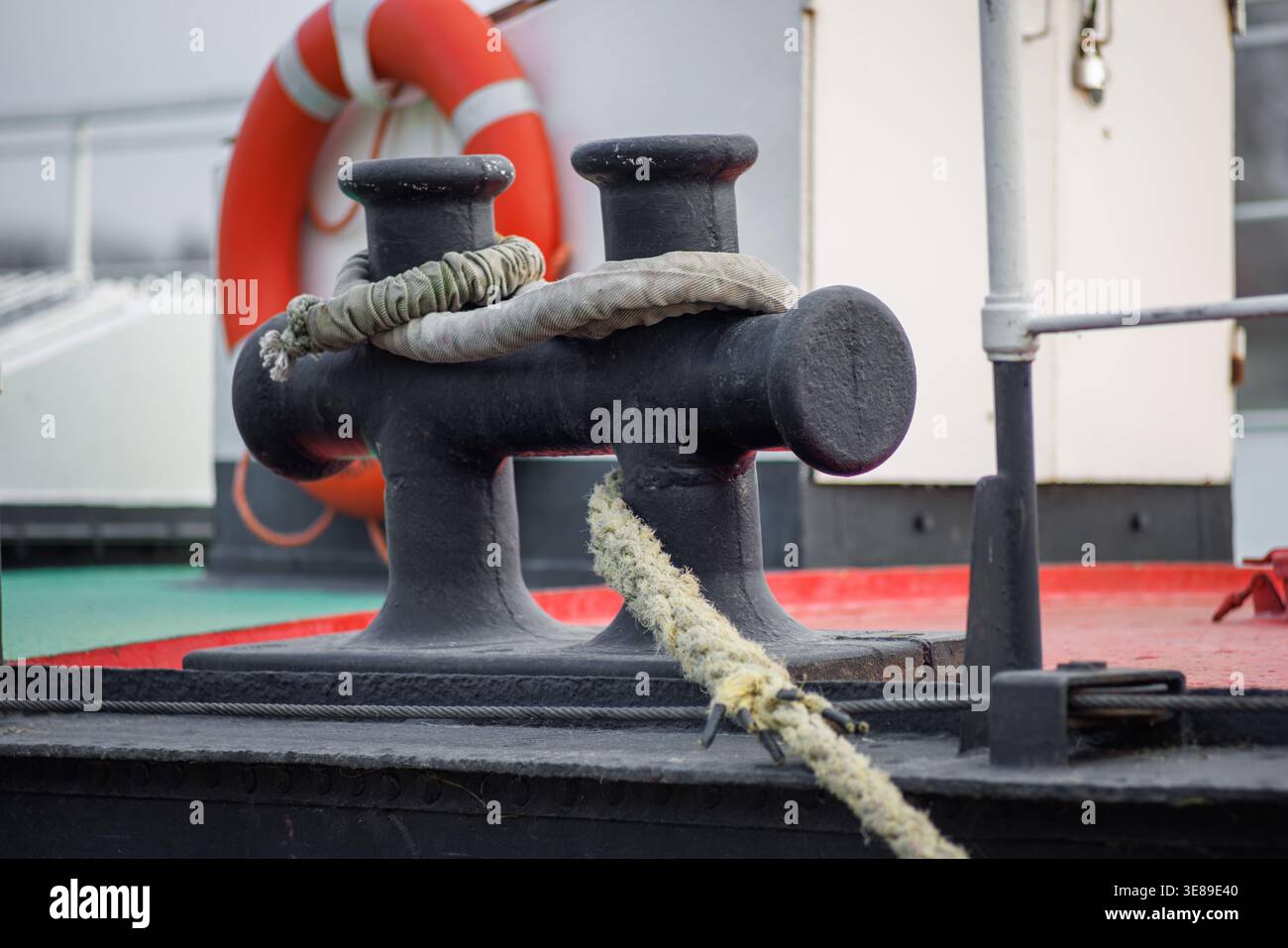 Ein doppelter Schiffspoller mit einem Seil, das an ihm befestigt ist, vor dem Hintergrund eines Rettungsrufs auf einem Schiff. Schiffsverankerung. Stockfoto