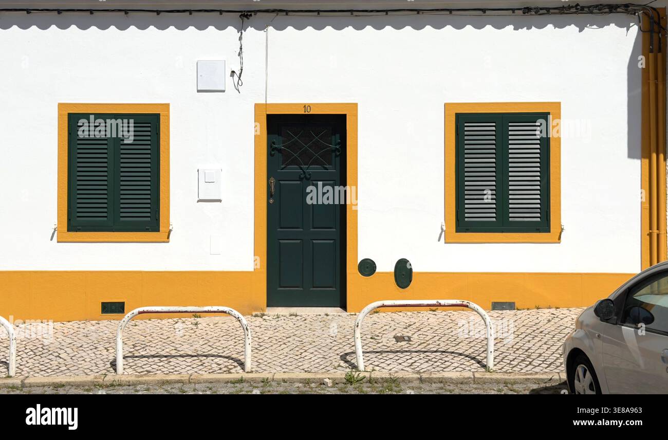 Traditionelle portugiesische Hausfassade mit weißen Wänden, gelben Zierleisten, grünen Türen und Fensterläden in der Region Alentejo Ferragudo Stockfoto