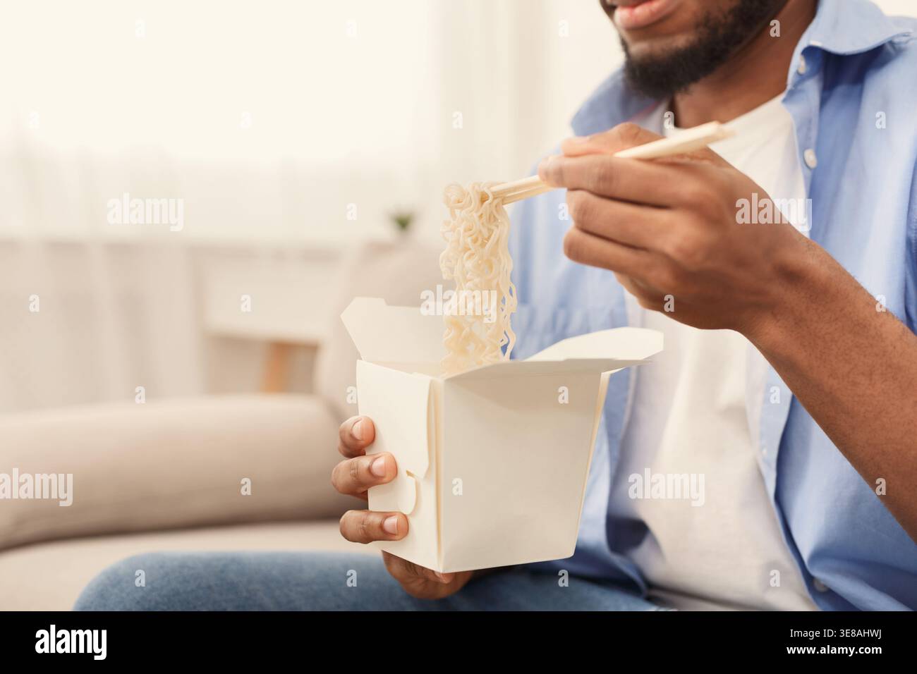 Junger afroamerikanischer Mann, der zu Hause asiatisches Essen isst Stockfoto