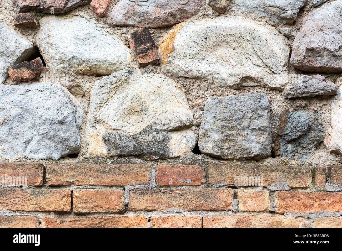 Aus nächster Nähe sehen Sie eine strukturierte Steinmauer aus grauen Steinen und roten Ziegeln, die die rustikalen Details und den Mörtel für den Bau hervorhebt Stockfoto