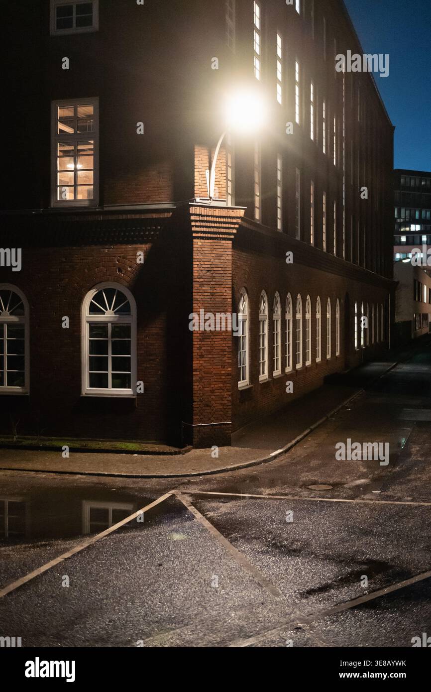 Straßenecke aus braunem Backsteingebäude bei Nacht. Ein klassisches Ziegelgebäude, beleuchtet durch eine helle Straßenlaterne bei Nacht, mit nassem Bürgersteig. Stockfoto