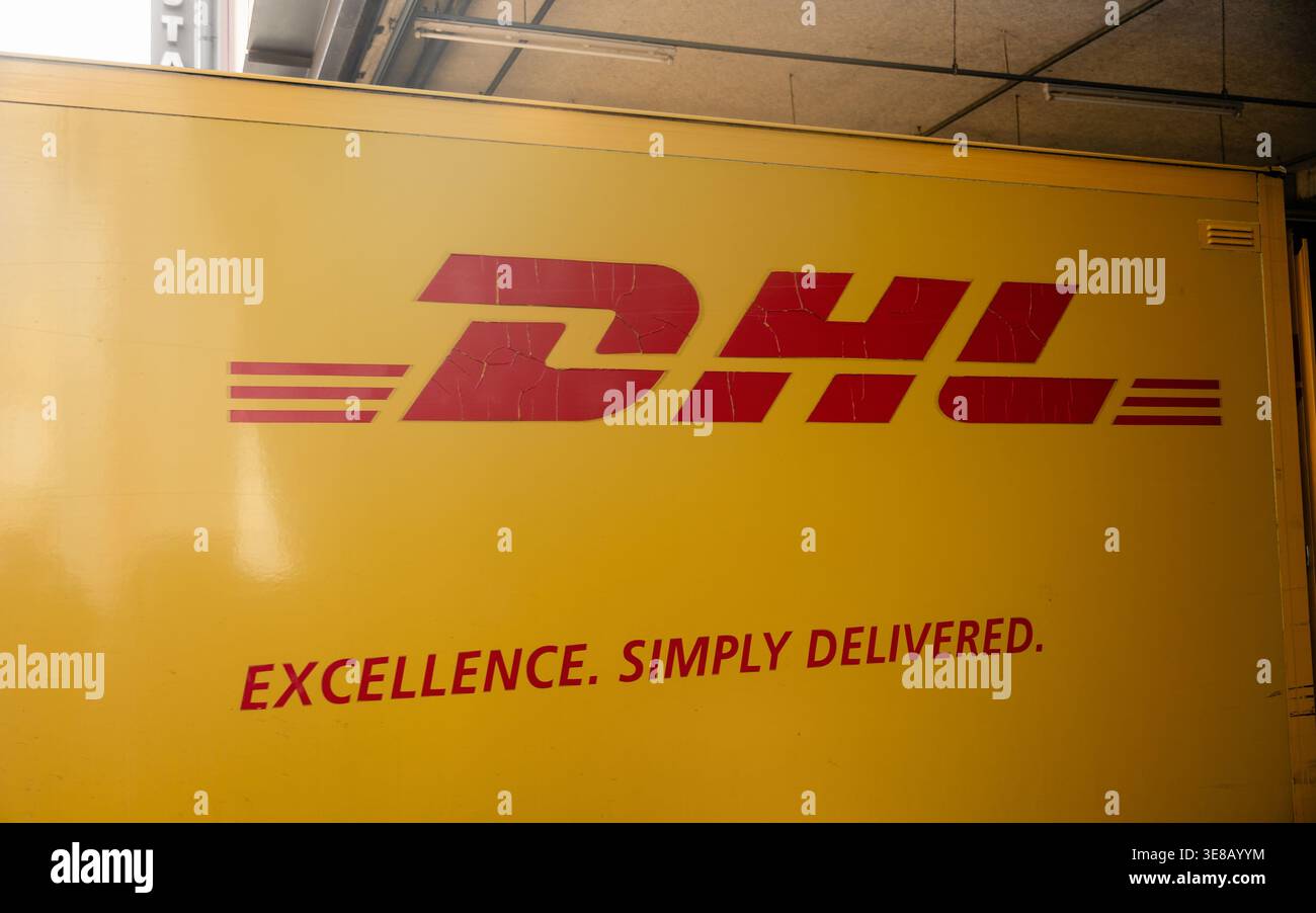 DHL-Lieferwagen parkt an der Laderampe. Gelber Kastenwagen mit DHL-Logo – Seitenansicht des gelben Anhängers, der unter dem Gebäudeüberhang geparkt ist. Stockfoto