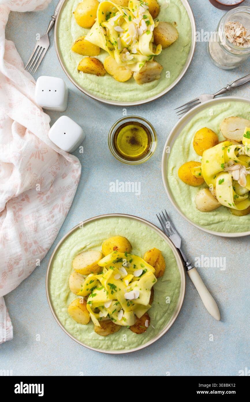 Gebackene Kartoffeln werden mit fermentierten Zucchini belegt und zusammen mit einer grünen Erbsensauce mit Brokkoli serviert. Diese Mahlzeit wird für ein gesundes Frühstück zubereitet Stockfoto
