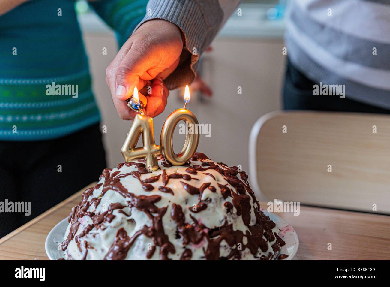 Bei einer kleinen Familienfeier zünden Sie goldene „40“-Geburtstagskerzen auf einem hausgemachten Schokoladen-Tropfkuchen an, um warme, intime Momente der Freude festzuhalten, m Stockfoto