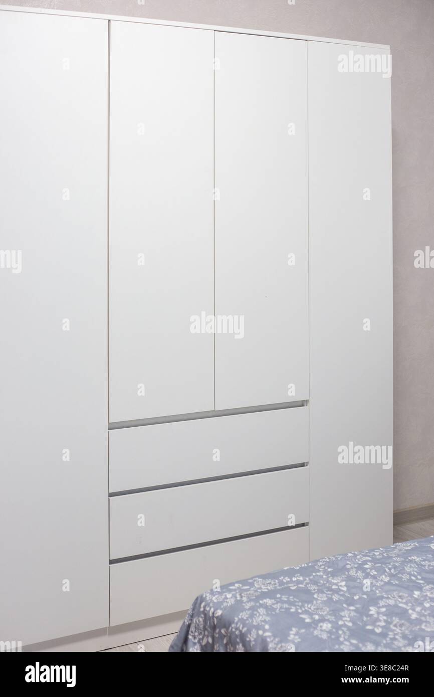 Moderner weißer Kleiderschrank mit drei Schubladen und vier Türen in einem Schlafzimmer. Inneneinrichtung, Möbel, Wohnkultur, Stauraum Stockfoto