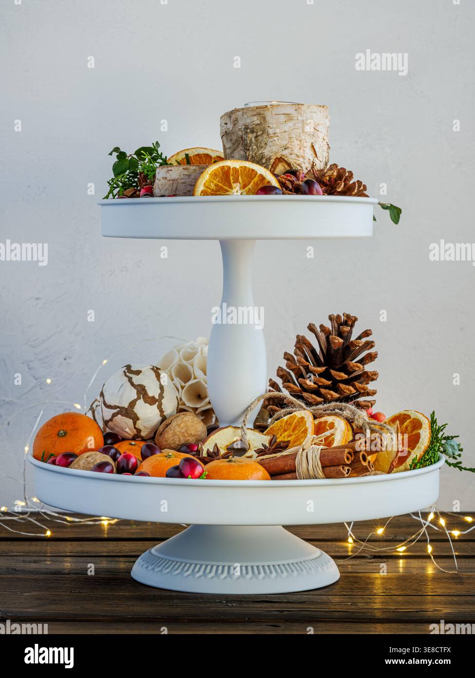 Herbst festliche Weihnachtsdekoration weißes Tablett mit Birkenrindenkerzen, Tannenzapfen, Preiselbeeren, Walnüssen, Orangen, Feenlichter auf rustikalem Plankenholz Stockfoto