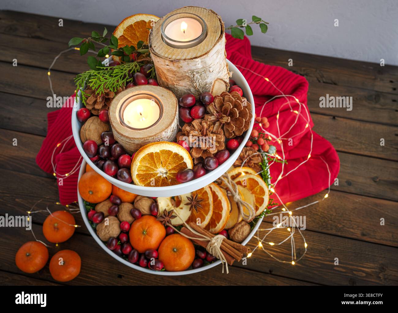 Herbst festliche Weihnachtsdekoration weißes Tablett mit Birkenrindenkerzen, Tannenzapfen, Preiselbeeren, Walnüssen, Orangen, roter Pullover und Feenlichter Stockfoto
