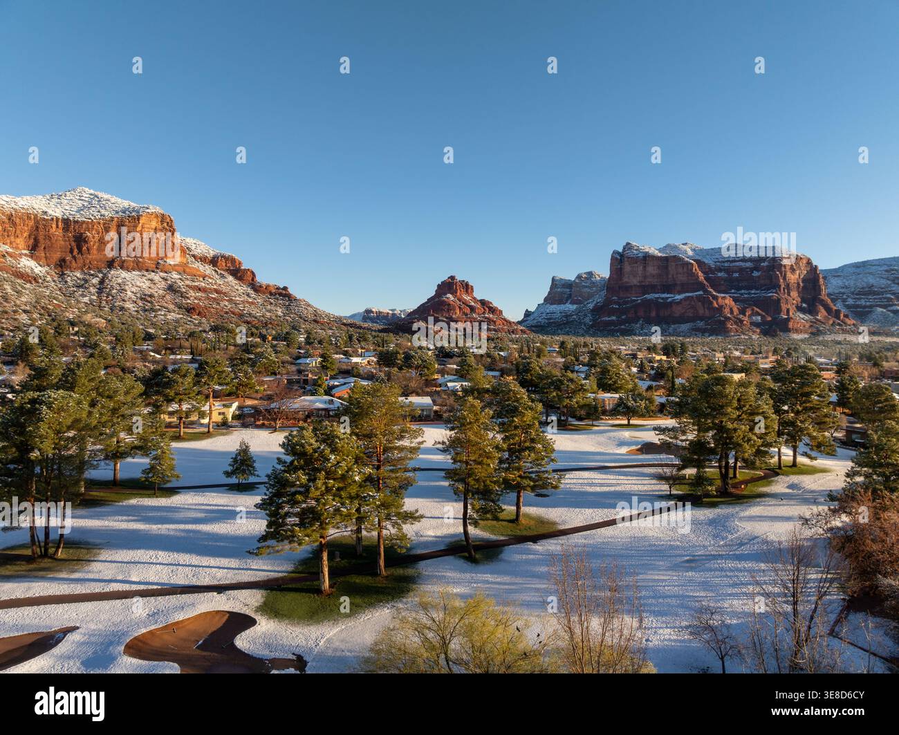 Schneebedeckter Golfplatz mit Kiefern und roten Felsenbergen in Sedona Arizona unter klarem, blauem Winterhimmel aus der Vogelperspektive. Stockfoto