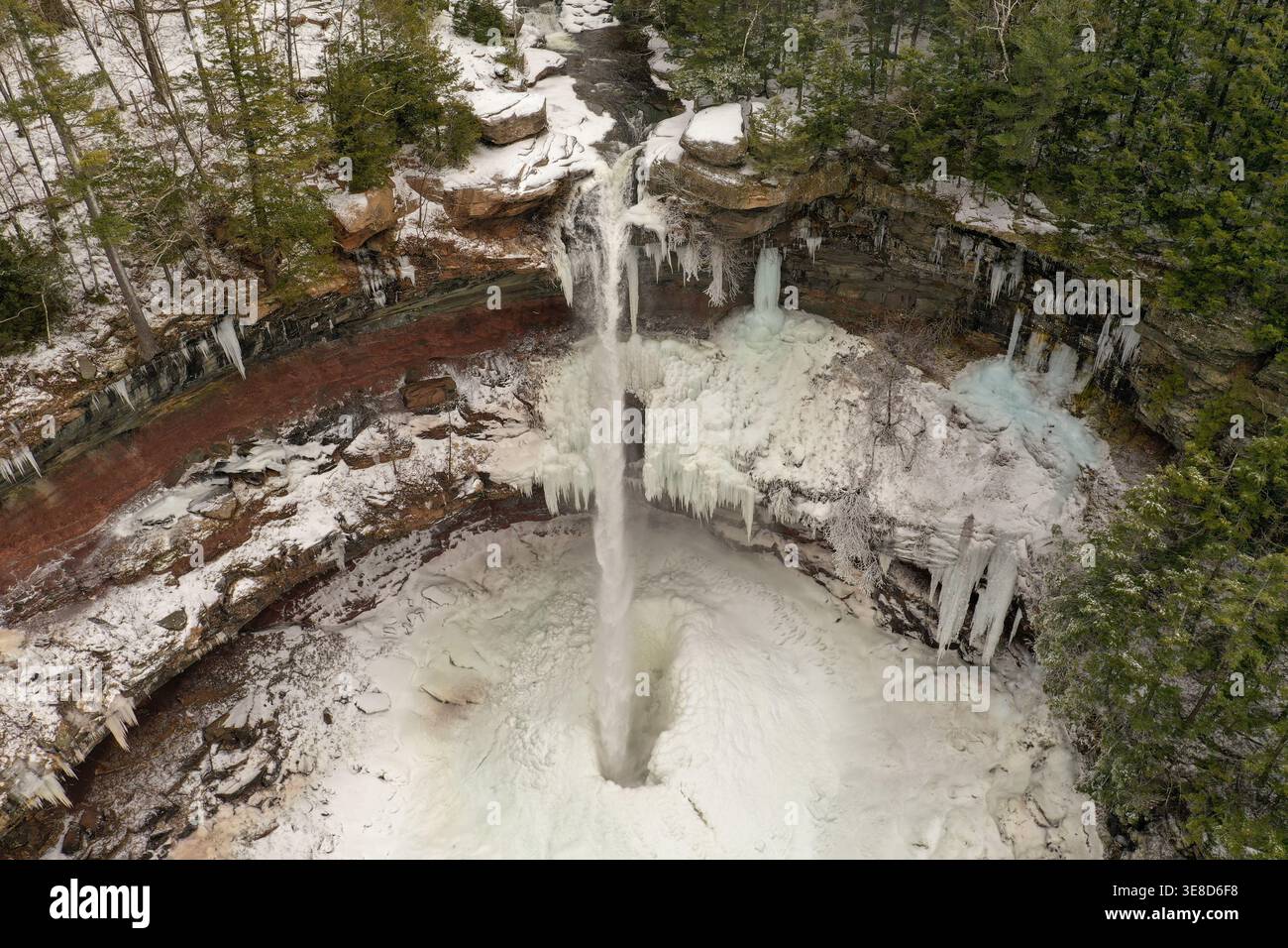 Gefrorener Wasserfall, der im Winter in eine bewaldete Schlucht in der Nähe von Ithaca New York mit riesigen Eiszapfen und schneebedeckten Klippen eintaucht. Stockfoto