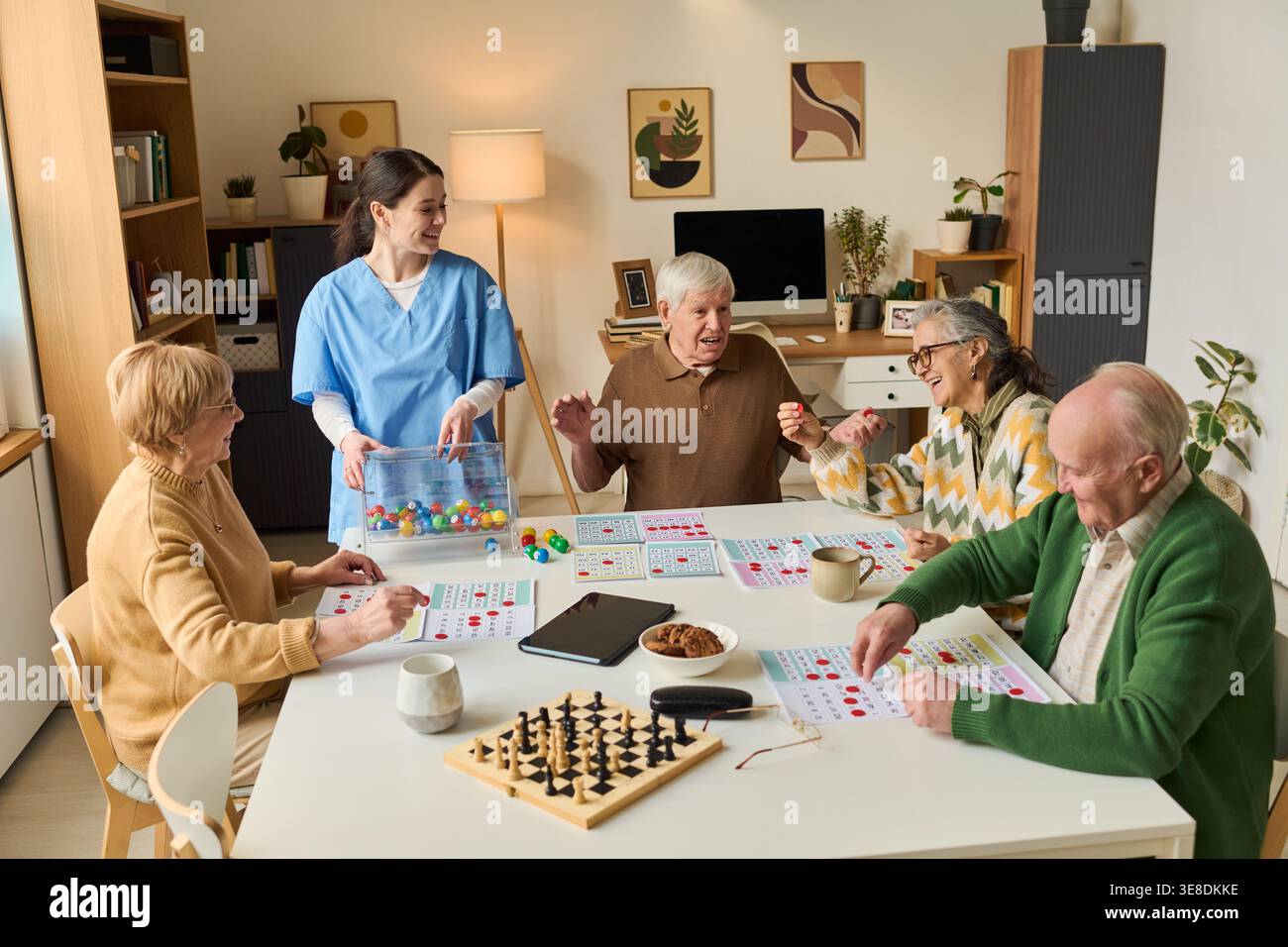 Seniorengruppe, die kognitive Spiele mit weiblichen Betreuerinnen in Pflegeheimen spielt, Gedächtnistraining und soziales Engagement unterstützt. Ideal für Altenpflege, Demenzunterstützung, Senioren Wellness Marketing Stockfoto