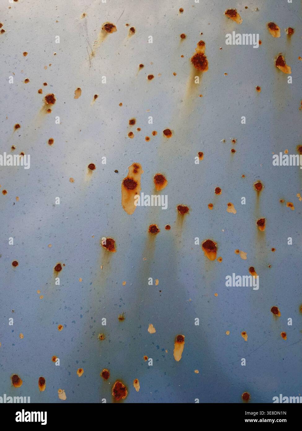 Eine detaillierte Ansicht der Oxidation auf einer hellblauen Metallplatte mit zahlreichen kleinen orange-braunen Rostflecken und vertikalen Tropfstellen von der Weather expo Stockfoto