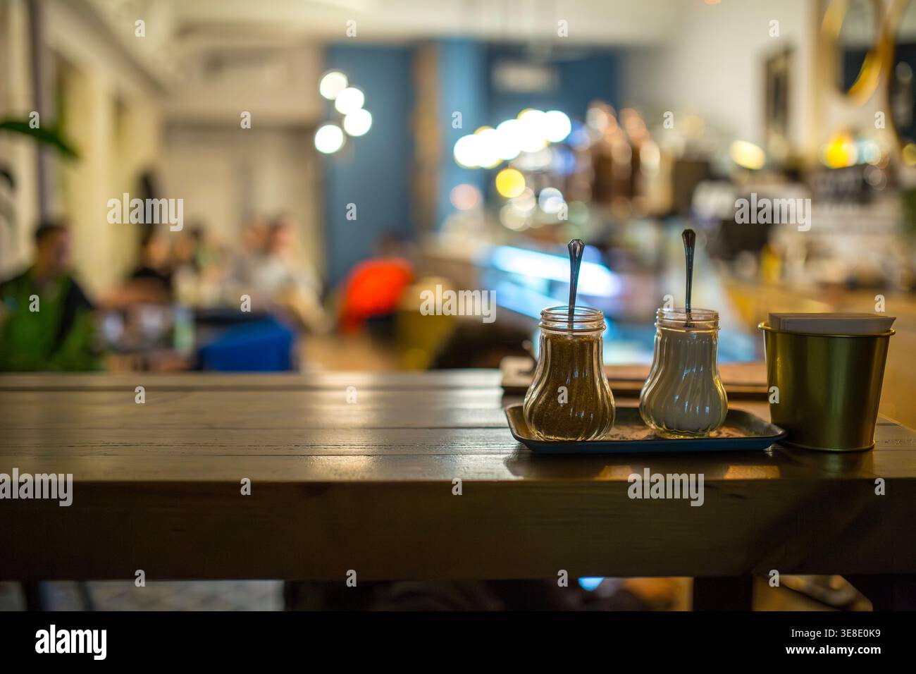 Nahaufnahme eines Cafés mit Zuckerspendern und Servietten. Der unscharfe Hintergrund zeigt warme Bokeh-Lichter und Besucher, die an eine entspannte, Invi erinnern Stockfoto