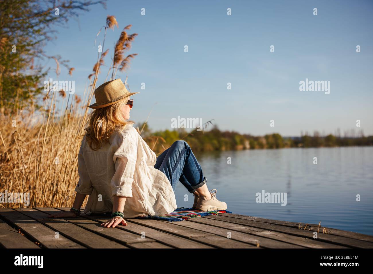 Frau, die sich am Pier am See entspannt. Ruhige Einsamkeit in der Natur, digitale Entgiftung und achtsames langsames Leben Stockfoto