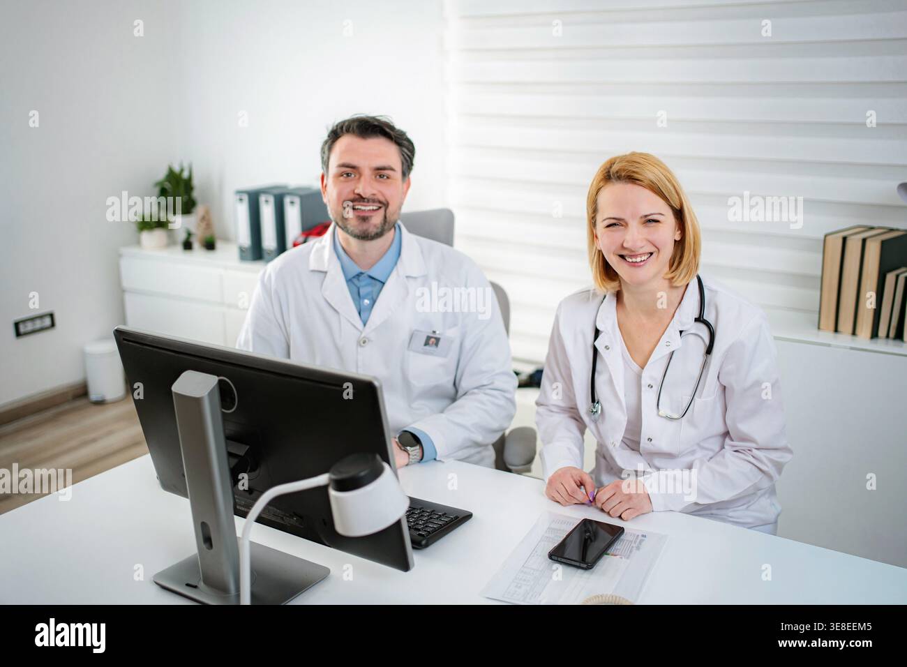 Zwei medizinische Fachkräfte sitzen an einem Schreibtisch und lächeln in einer Klinik Stockfoto