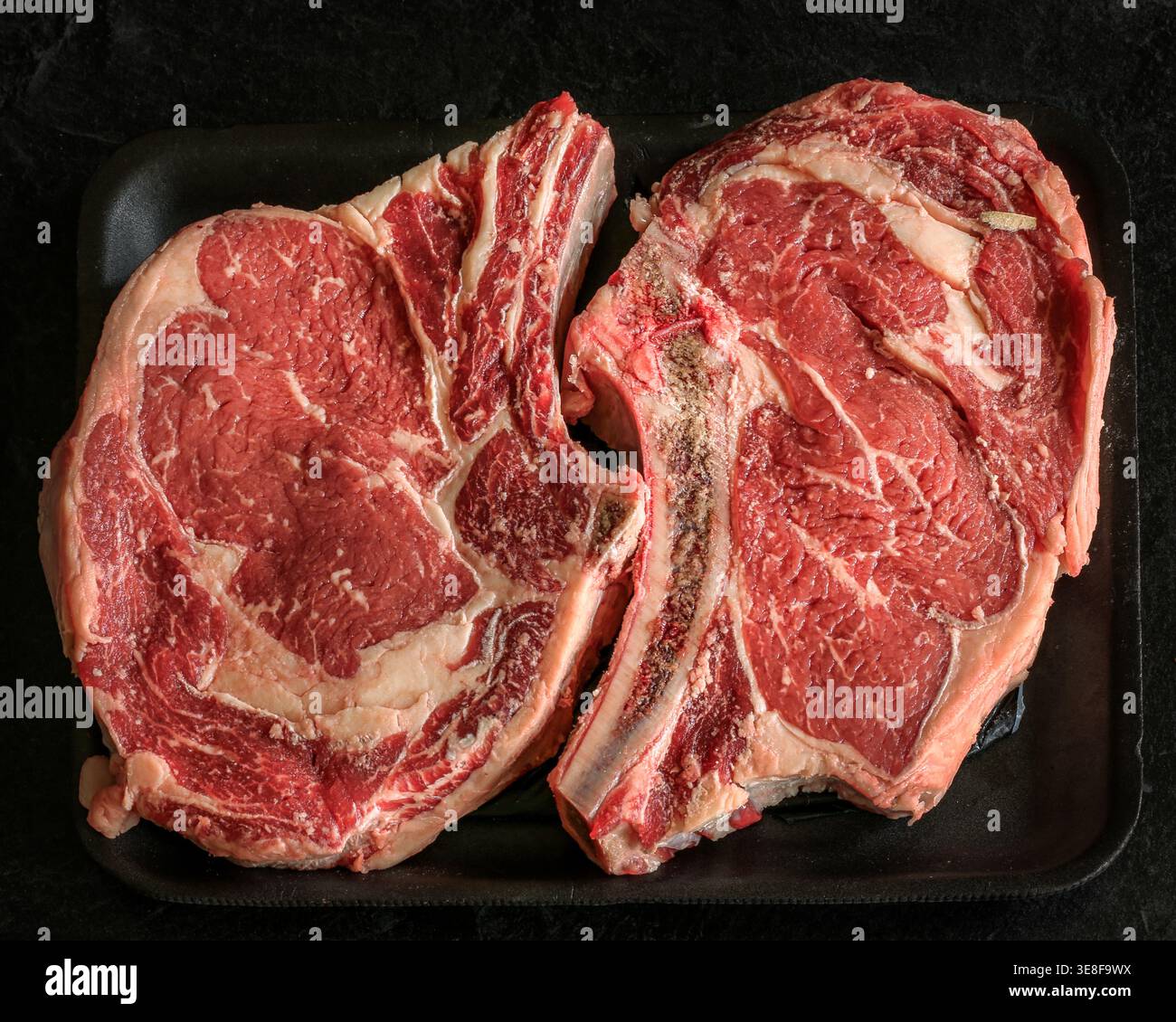 Frische Steaks mit Rippenaugen auf schwarzem Hintergrund. Stockfoto